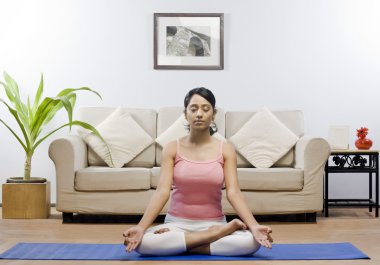 Woman meditating in a living room clipart