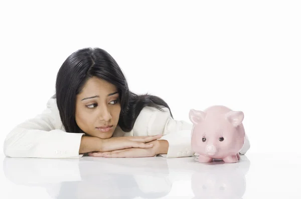 Mulher de negócios olhando para um banco porquinho — Fotografia de Stock