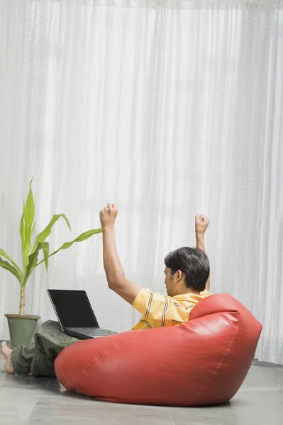 Man sitting on a bean bag in front of a laptop — Stock Photo, Image