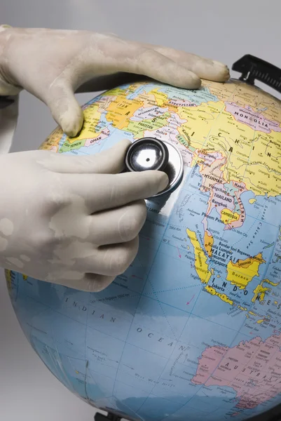 Hands examining a globe with a stethoscope — Stock Photo, Image