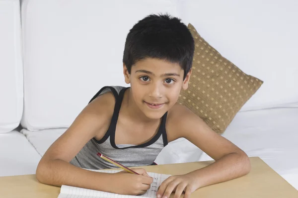 Boy sitting on a sofa and writing — Stock Photo, Image
