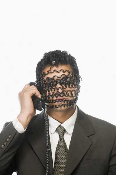 Empresário com o rosto coberto por cabo de telefone — Fotografia de Stock