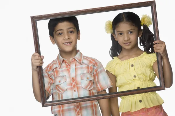 Chica y un niño sosteniendo un marco vacío — Foto de Stock