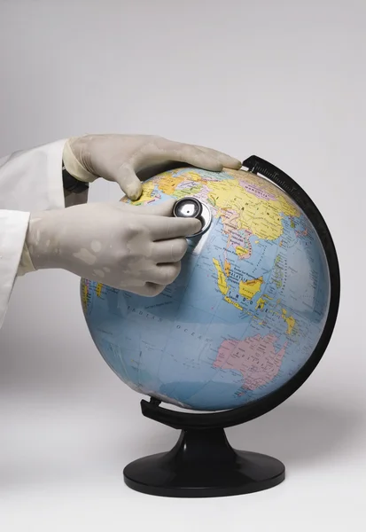 Les mains examinant un globe avec un stéthoscope — Photo