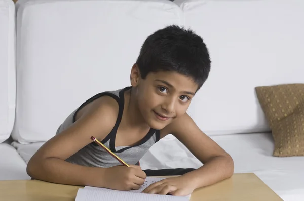 Boy sitting on a sofa and writing — Stock Photo, Image