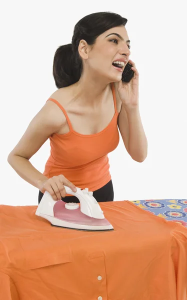 Vrouw strijken en praten op een mobiele telefoon — Stockfoto