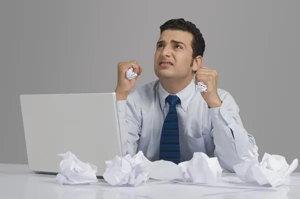Geschäftsmann schaut besorgt mit zerknüllten Papieren auf Schreibtisch — Stockfoto