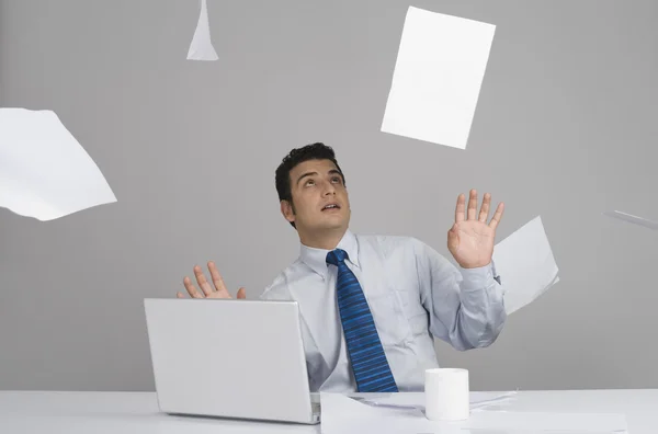 Businessman sitting in office with papers falling around him — Stock Photo, Image