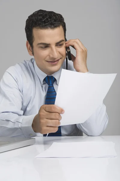 Empresario sosteniendo un documento y hablando por teléfono móvil —  Fotos de Stock