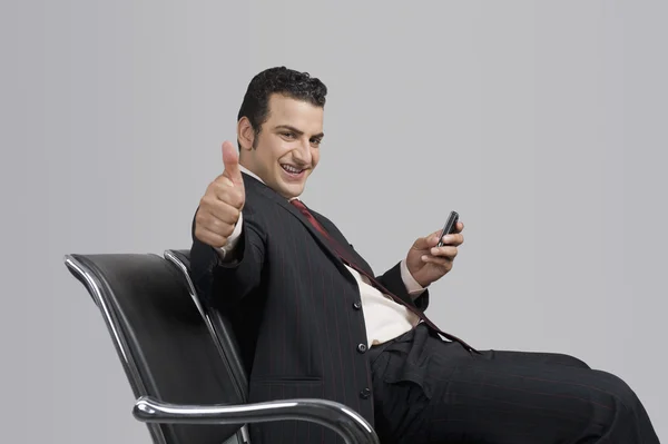 Businessman holding a mobile phone and showing thumbs up sign — Stock Photo, Image