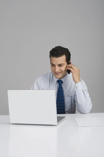 Empresário usando um laptop e falando em um telefone celular — Fotografia de Stock