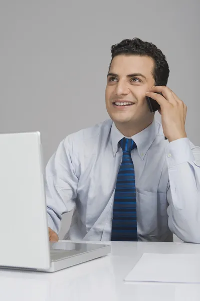 Businessman using a laptop and talking on a mobile phone — Stock Photo, Image