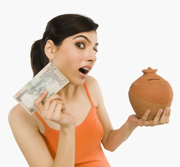 Woman holding notes with a piggy bank — Stock Photo, Image