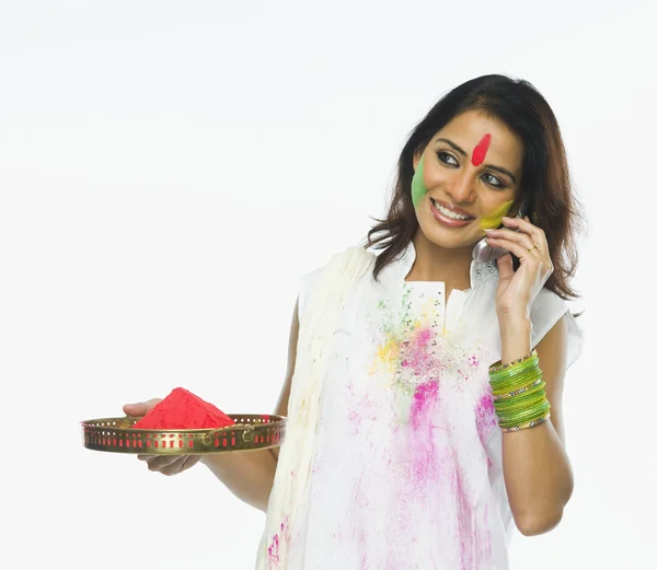 Woman holding Holi colors and talking on a mobile phone — Stock Photo, Image