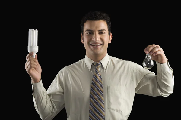 Empresario comparando una bombilla con una bombilla de bajo consumo — Foto de Stock