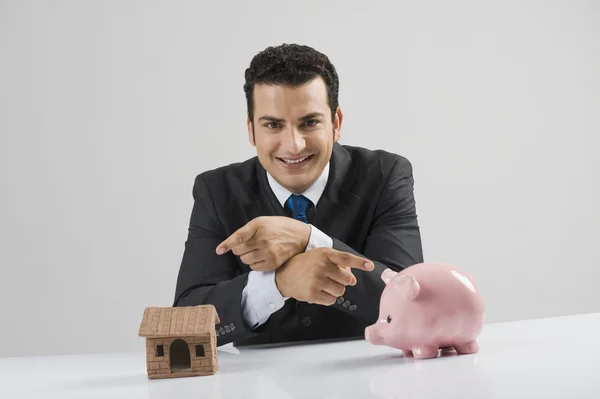 Businessman with a model home and a piggy bank — Stock Photo, Image