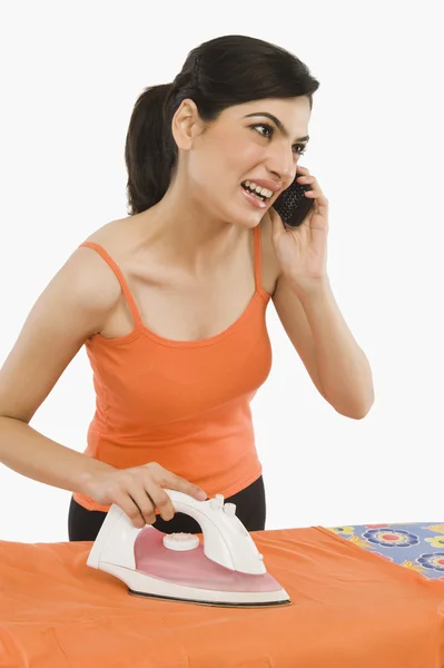 Vrouw strijken en praten op een mobiele telefoon — Stockfoto