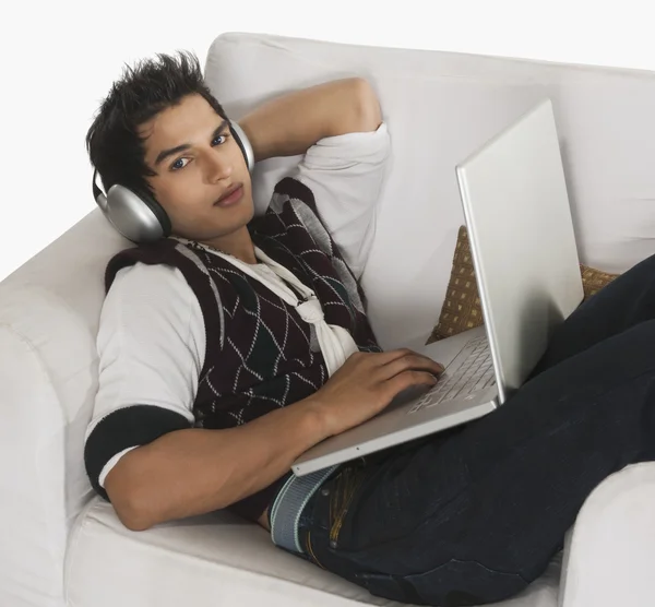 Man listening to headphones while using a laptop — Stock Photo, Image