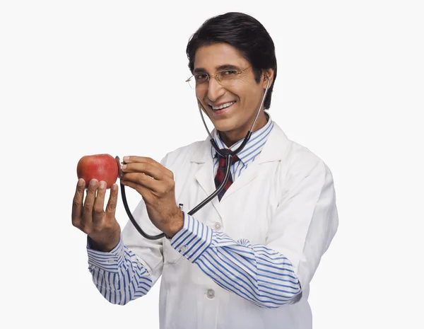 Доктор слушает яблоко со стетоскопом — стоковое фото