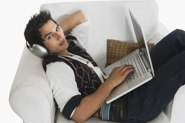 Man listening to headphones while using a laptop — Stock Photo, Image