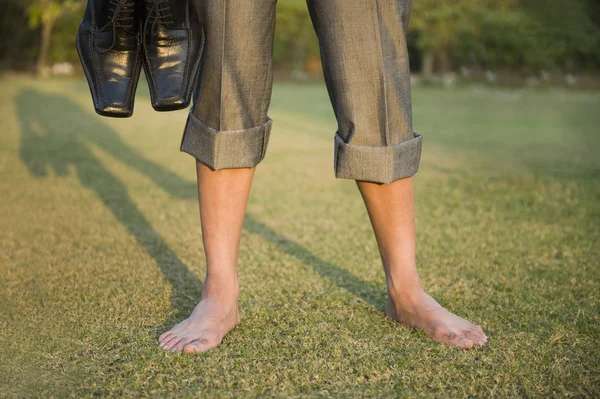 Empresário segurando sapatos em um parque — Fotografia de Stock