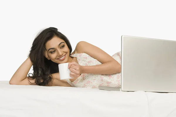 Frau liegt mit Kaffeebecher auf dem Bett — Stockfoto
