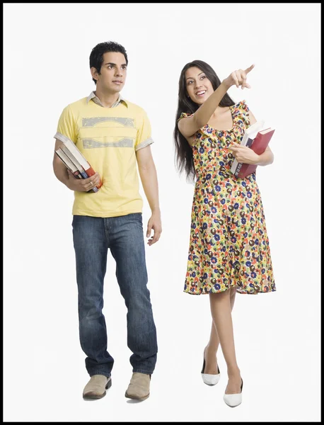 Woman holding books and pointing away beside her boyfriend — Stock Photo, Image