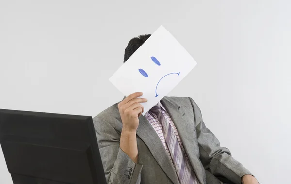 Empresário segurando um papel sorridente na frente de seu rosto — Fotografia de Stock