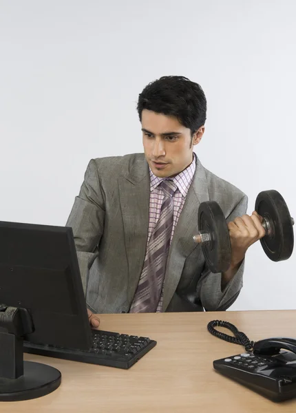 Businessman exercising with dumbbells and working on a computer — Stock Photo, Image