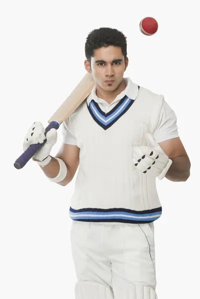 Cricket batsman holding a bat and tossing a ball — Stock Photo, Image