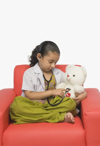 Chica examinando un oso de peluche con un estetoscopio — Foto de Stock