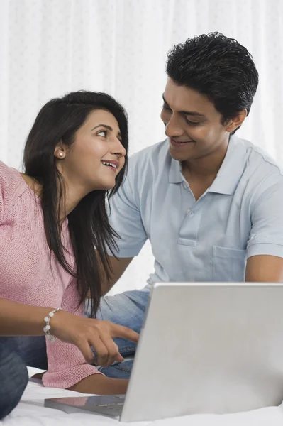 Casal sorrindo na frente de um laptop na cama — Fotografia de Stock