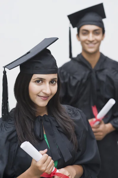 Couple in graduation gowns holding diplomas — Stock Photo, Image
