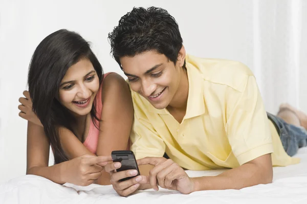 Casal olhando para um telefone celular na cama — Fotografia de Stock