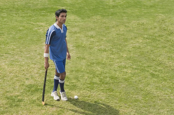 Hombre sosteniendo un palo de hockey en un campo — Foto de Stock