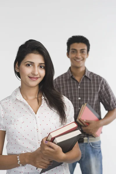 Woman holding books with her friend in the background — Stock Photo, Image