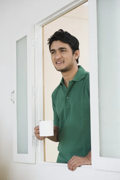 Man standing at a window holding a cup of coffee — Stock Photo, Image