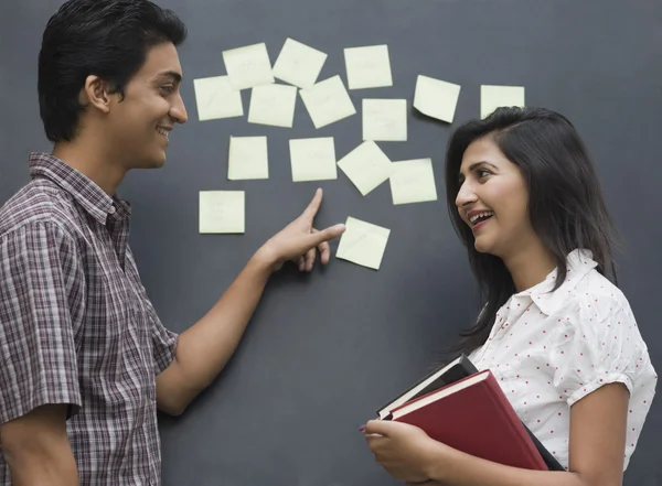 Estudantes universitários sorrindo na frente de um quadro de avisos — Fotografia de Stock