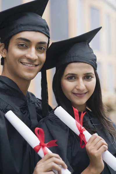 Couple in graduation gowns holding diplomas — Stock Photo, Image