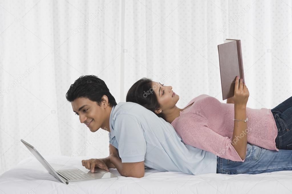 Man using a laptop and his girlfriend reading a book