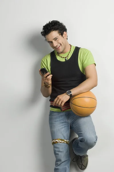 Homem segurando uma bola e usando um telefone celular — Fotografia de Stock