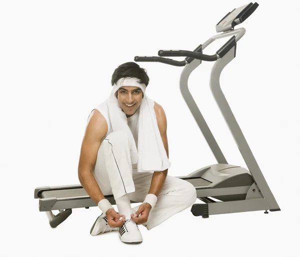 Man sitting on a treadmill and tying shoelaces — Stock Photo, Image