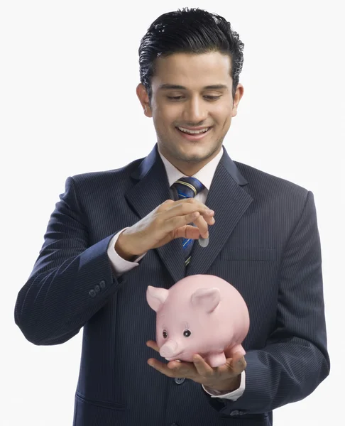 Empresario poniendo una moneda en una alcancía — Foto de Stock