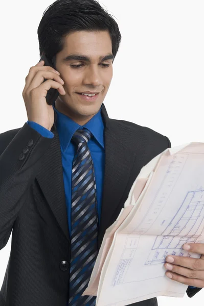 Real estate agent holding a blueprint and talking on a mobile phone — Stock Photo, Image