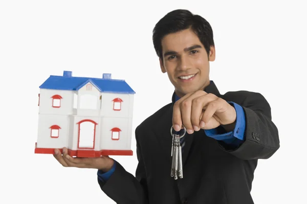 Real estate agent holding house keys and a model home — Stock Photo, Image