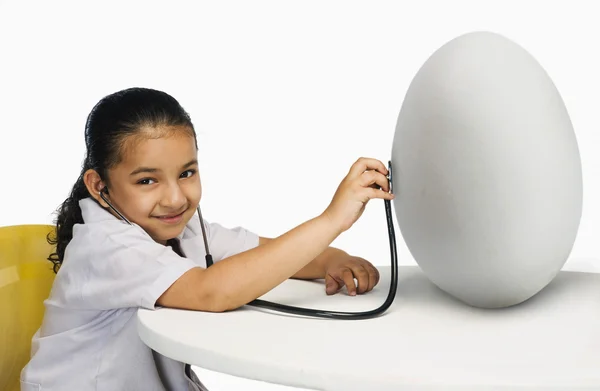 Girl examining a egg with a stethoscope — Stock Photo, Image