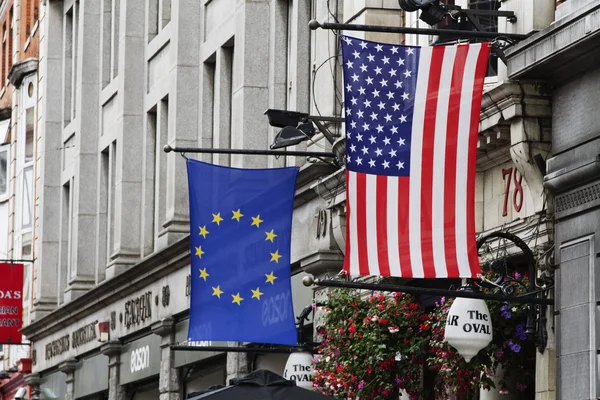 Bandera americana y bandera de la Unión Europea colgando en frente de un edificio —  Fotos de Stock
