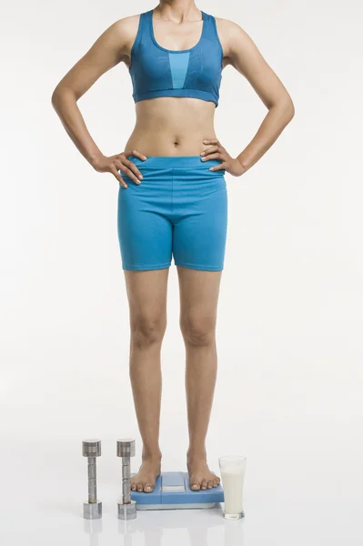 Mujer de pie en una escala de peso con brazos akimbo — Foto de Stock