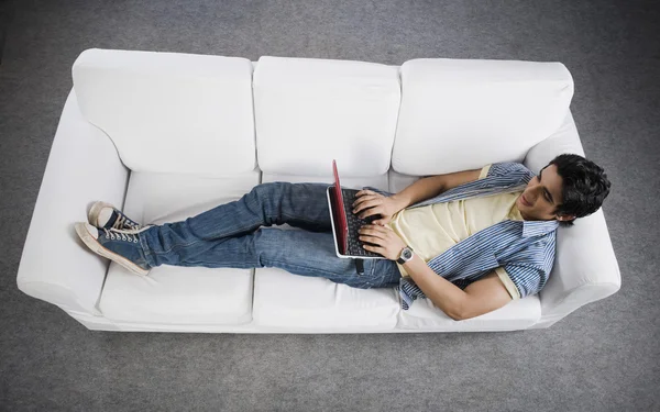 Mann liegt auf einem Sofa und arbeitet an einem Laptop — Stockfoto