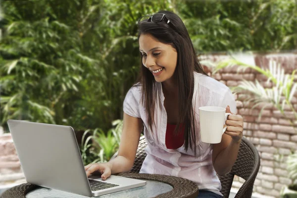 Mujer bebiendo café y usando un portátil — Foto de Stock